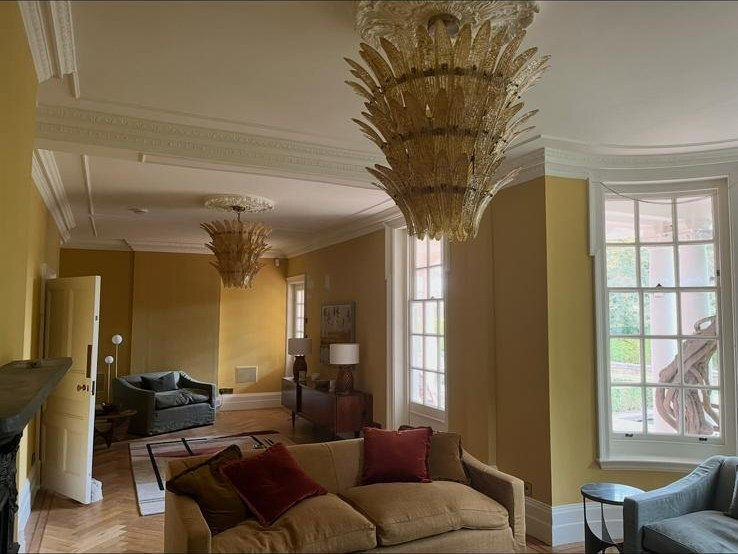 Decorated reception room with ochre walls, chandeliers and white cornicing