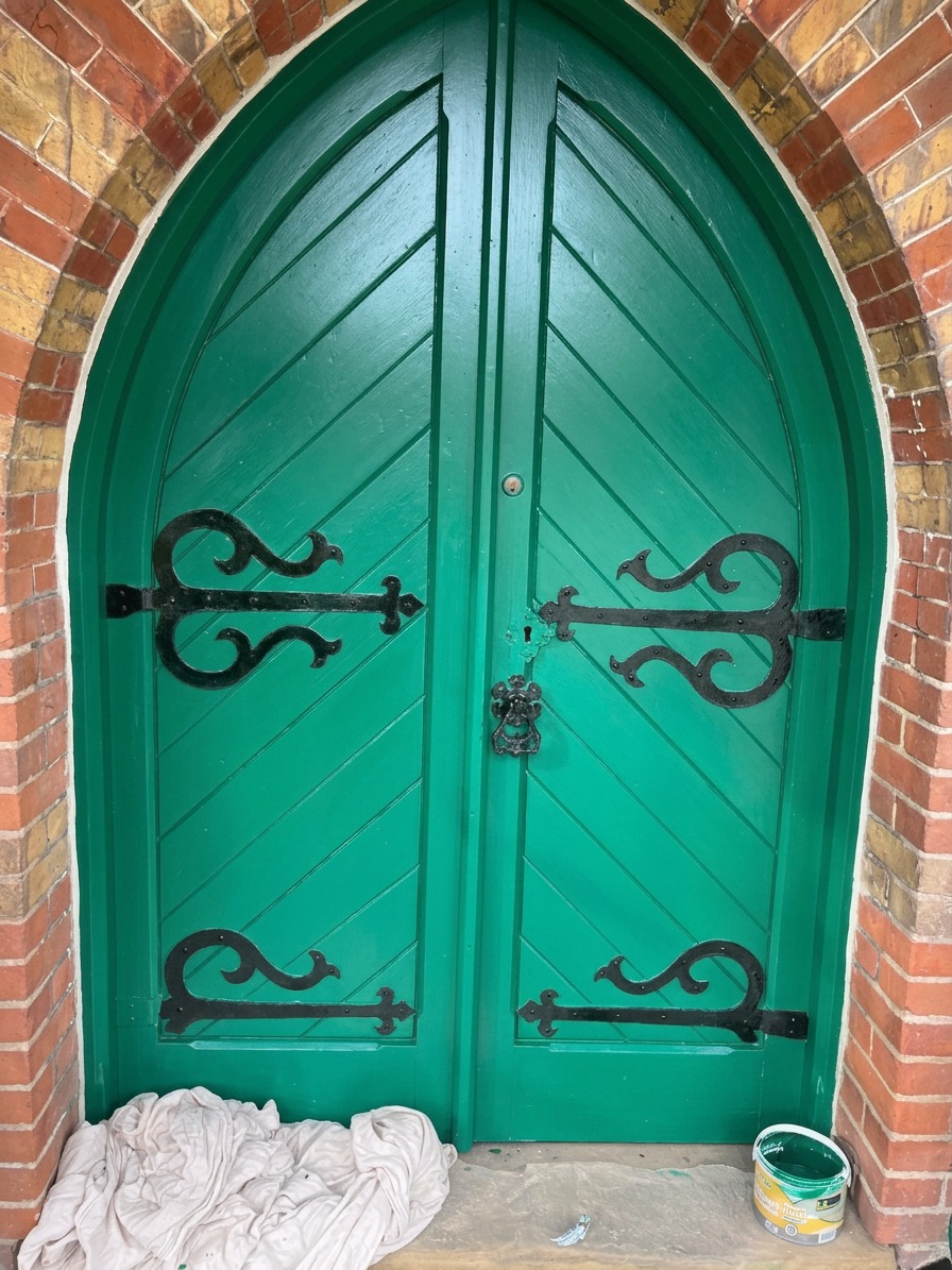 Freshly painted green arched timber doors with black ironmongery