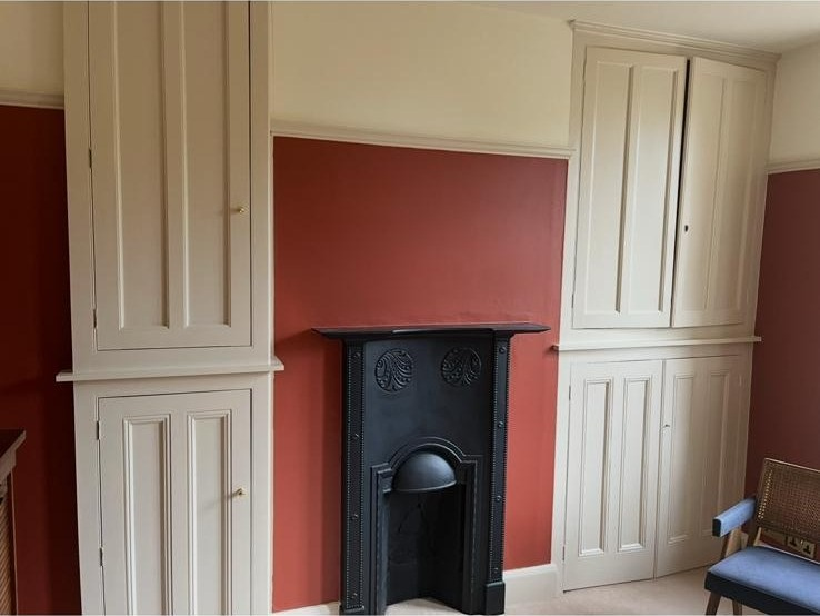 Terracotta feature wall with cream fitted joinery and black cast-iron fireplace